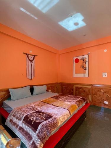 Bett in einem Zimmer mit orangefarbener Wand in der Unterkunft Trippy Trails in Kasol