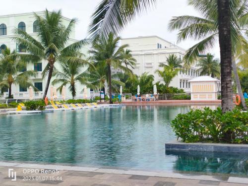 a swimming pool with palm trees in front of a building at V&T Hotel Phu Quoc - 3 minutes to Beach in Phú Quốc