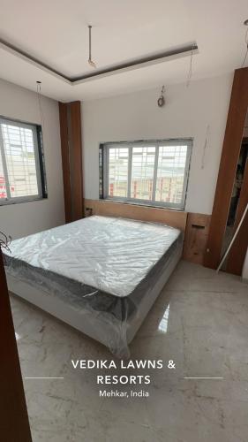 een slaapkamer met een bed in een kamer met ramen bij Vedika Hotel in Mehekar