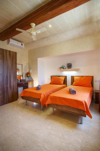 a bedroom with two beds with orange pillows at Carini Farmhouses in Għarb