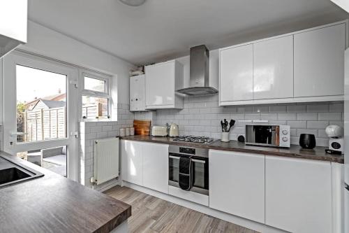a white kitchen with white appliances and a window at Tiger House - Driveway & Garden. Airport location! in Luton