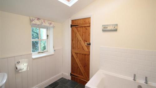 Mulberry Hill Cottage في Nicholaston: حمام مع حوض استحمام أبيض وباب خشبي