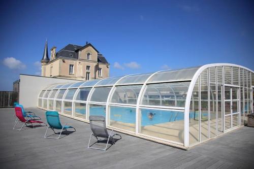 a glass building with chairs and a swimming pool at Les Tourelles Village de vacances in Asnelles