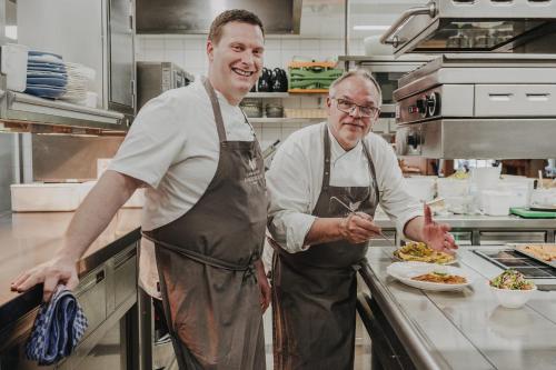 two men standing in a kitchen preparing food at Buchnas Landhotel Saarschleife in Mettlach