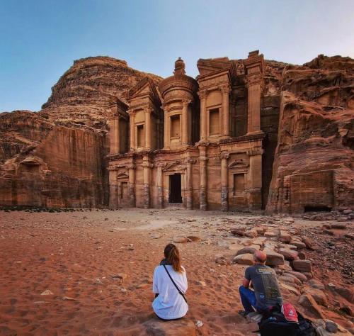 a man and a woman sitting in front of a rock building at cabin hotel in Ma‘ān