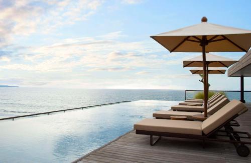 a row of lounge chairs with umbrellas next to a swimming pool at Alila Seminyak in Seminyak