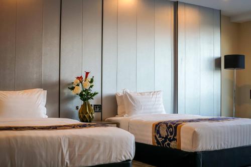 two beds in a hotel room with a vase of flowers at Hevea Hotel & Resort in Angeles