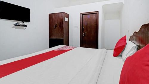 a bedroom with a white bed with red pillows and a television at Backpackers Dinesh Home Stay in Khajurāho