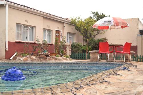 una piscina con tavolo e due sedie rosse e ombrellone di Sunflower Cottage 15min from OR Tambo a Johannesburg