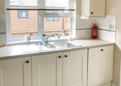 a white kitchen with a sink and a window at Whitecairn Holiday Park in Glenluce