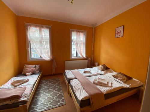 two beds in a room with orange walls and windows at Penzion Jáchymov Pod Lanovkou in Jáchymov