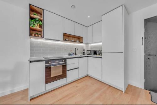 uma cozinha com armários brancos e electrodomésticos de aço inoxidável em Colindale NW9 1BED TV/WIFI em Colindale