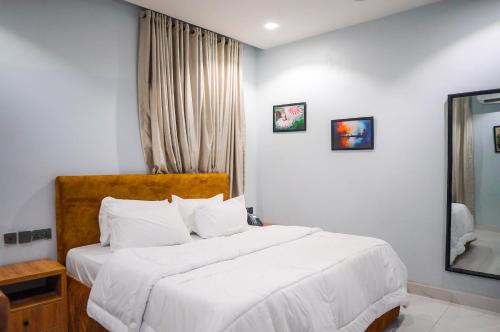 a bedroom with a bed with white sheets and a mirror at Cedarwood Apartments in Abuja