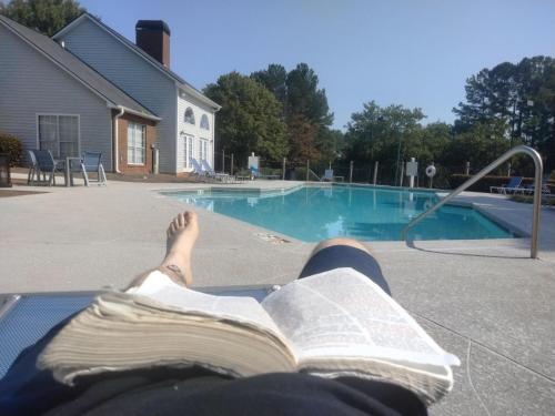 una persona leyendo un libro junto a una piscina en Slinger Suites en Hendersonville