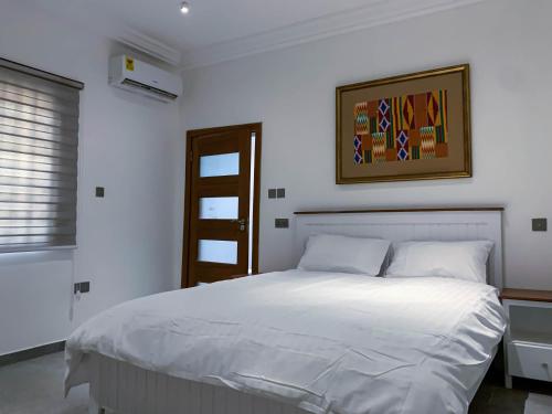 Un dormitorio con una cama blanca con una foto en la pared en Cony’s Guest House, en Kwabenyan