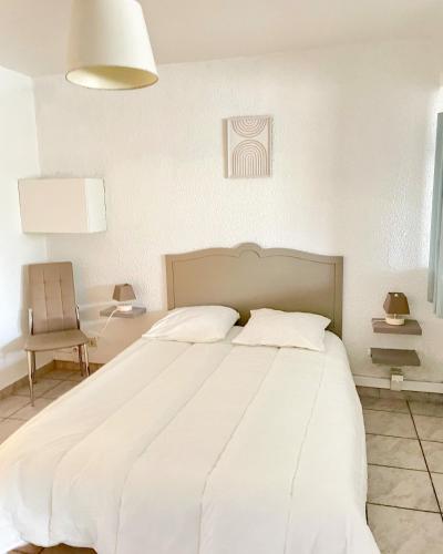 ein weißes Bett in einem weißen Schlafzimmer mit einem Stuhl in der Unterkunft Le cocon in Eugénie-les-Bains