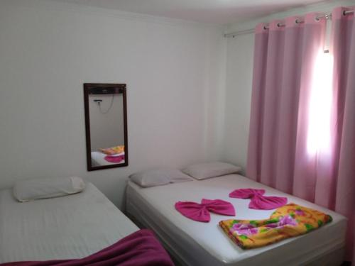 Duas camas num quarto com cortinas cor-de-rosa e um espelho. em Hotel da Creuza em Goiânia