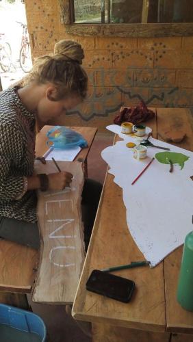 a woman sitting at a wooden table working on a painting at Deniyaya National backpackers hostel in Deniyaya