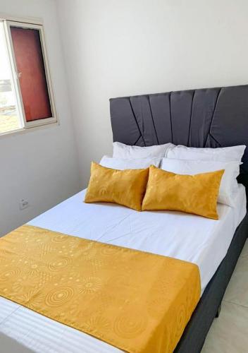 1 cama con sábanas blancas y almohadas amarillas en Acogedor Apartaestudio cerca al aeropuerto, en Cúcuta