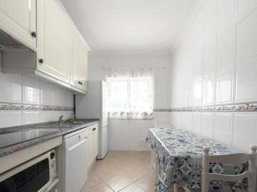 a white kitchen with a table and a window at Os Apartamentos A Ramos na Praia da Galé Estão inserido em Condomínio com PISCINA, Fica apenas a 350 Metros da Praia da Galé - Apartamentos com Ar Condicionado tanto nos Quartos como na Sala, Smart TV com Prime Vídeo e Cozinha Completa in Albufeira