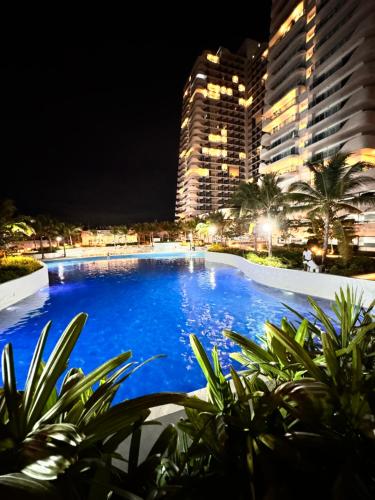 una piscina por la noche con edificios altos en LuxeBali Azure @ Azure North en San Fernando