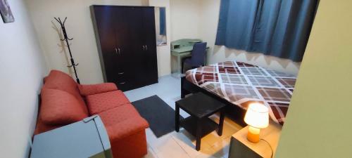 una pequeña sala de estar con sofá rojo y cama en Cozy Bedroom for Gent, en Sharjah