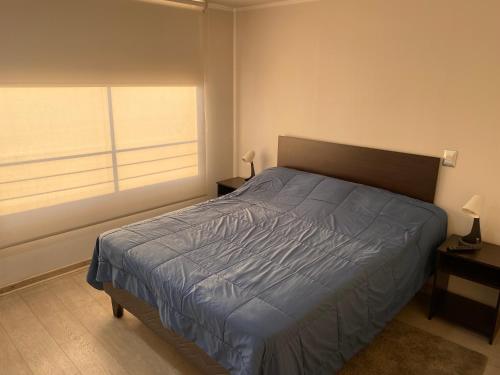 a bedroom with a bed with a blue comforter and a window at Amoblados MyK Metro Irarrazabal in Santiago