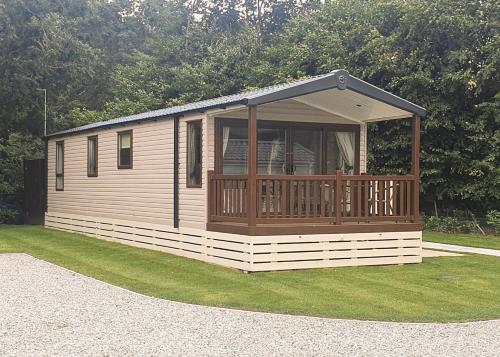 a large wooden cabin with a deck on the grass at Hamlet Rise in Leven