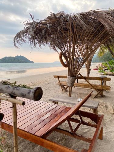 a wooden bench on the beach with a umbrella at BaanYaiGuesthouse in Ko Mak
