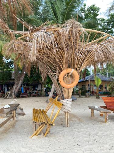 a beach with benches and a straw umbrella and a chair at BaanYaiGuesthouse in Ko Mak