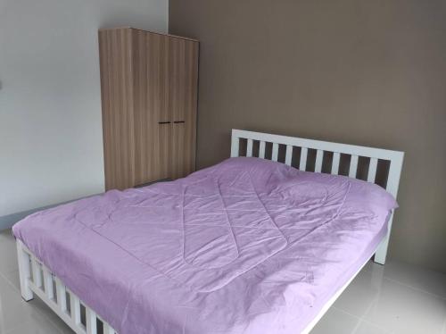 a bed with a purple comforter and a wooden cabinet at Flourish Homes ฟลอริชโฮมส์ ห้องพัก มอเกษตร สกลนคร in Ban Na Oi