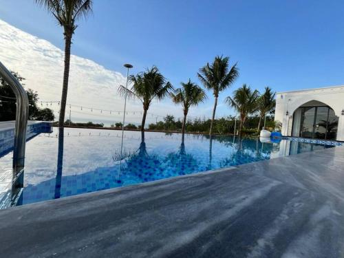 a swimming pool with palm trees and a building at Amanda villa 4 Phan Thiết in Mui Ne