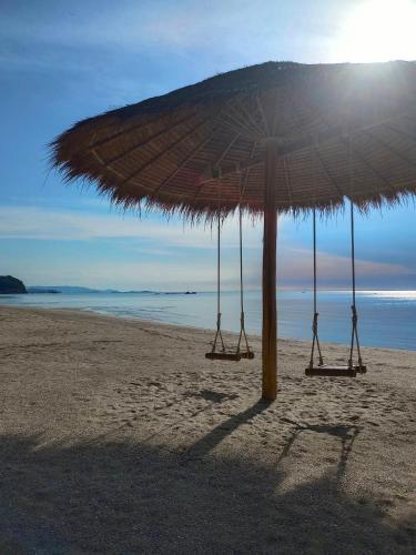 a large straw umbrella on a sandy beach at Chaithalay Khanom Resort in Ban Phang Phrao