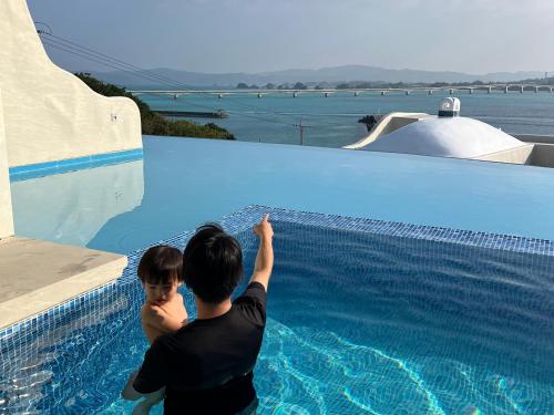 a man and a boy standing next to a swimming pool at Yuki Suite Kourijima in Nakijin