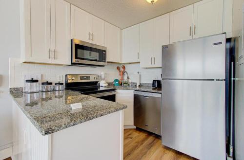 a kitchen with white cabinets and a stainless steel refrigerator at 0705 Palms That Sway by Atlantic Towers in Carolina Beach