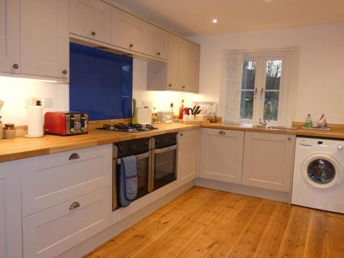 a kitchen with white cabinets and a washer and dryer at Cotswolds cottage near Stroud, with amazing views. in Brimscombe