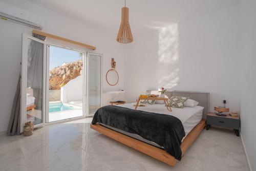 a white bedroom with a bed and a large window at Nèsoi Villas Naxos in Naxos Chora