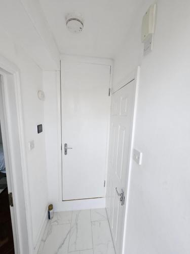 a white bathroom with a door and a white tile floor at Nice and Cosy One Bed Flat in Carshalton