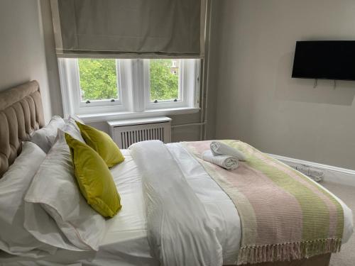 a bed with yellow and white pillows and a window at Central Park Aparthotel in London