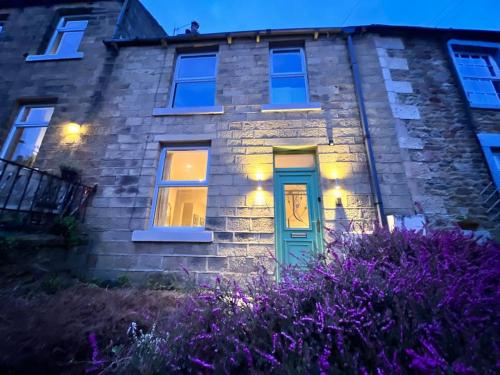 a stone house with a blue door and purple flowers at Arthur’s Cottage in Skipton