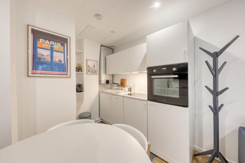 une cuisine avec des armoires blanches et un micro-ondes dans l'établissement L'Orée de Garnier I 1BR I 10 min from Opéra, à Paris