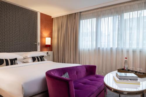 a hotel room with a large bed and a purple chair at Hôtel Etoile Maillot in Paris