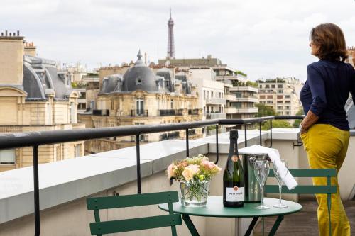 a woman standing on a balcony with a table with a bottle of wine at Hôtel Etoile Maillot in Paris