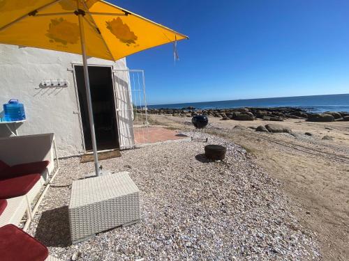 a yellow umbrella sitting on a beach next to the ocean at The Beach Shack Glamping & The Boat Shed in St Helena Bay