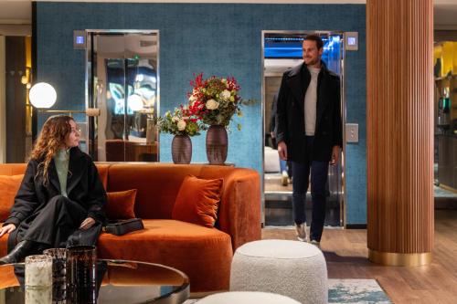 a man walking past a woman sitting on a couch in a lobby at Hôtel Etoile Maillot in Paris