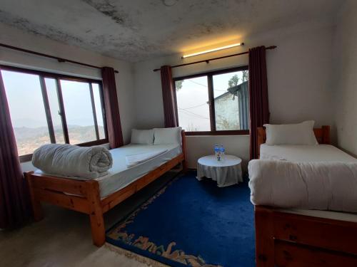 a room with two beds and a table and windows at Hotel Gogreen Kattike Pvt. Ltd. in Nagarkot