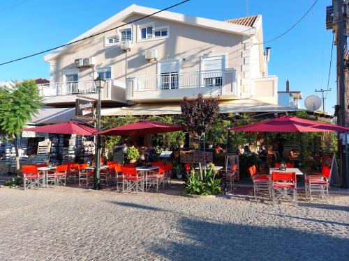 um café com mesas e cadeiras e guarda-sóis vermelhos em frente a um edifício em Skala Pearls A2 em Skála Kefalonias