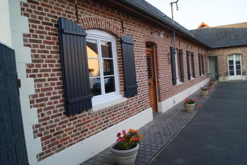 un edificio de ladrillo con ventanas negras y flores en ollas en La longère de Suzanne, en Arrest