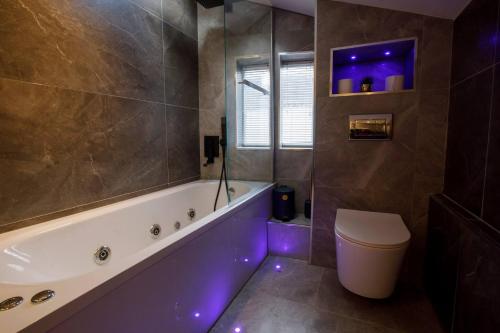 ein Badezimmer mit einer Badewanne, einem WC und lila Leuchten in der Unterkunft Best Beach Side Family Flat, Central Weymouth! in Weymouth
