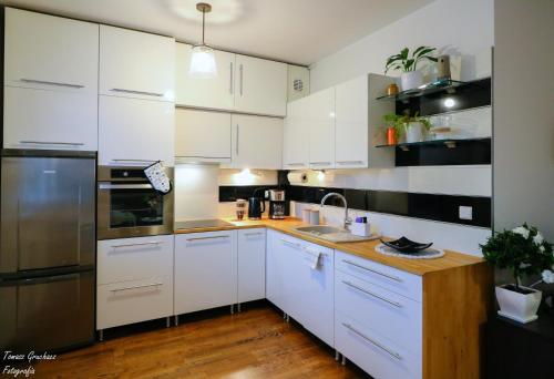 una cocina con armarios blancos y electrodomésticos de acero inoxidable en Apartament Działkowa przy Parku, en Chorzów